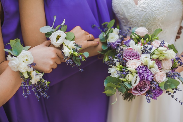 Close up of floral compositions worn around wrists of bridesmaids matching perfectly to bridal bouquet of flowers. Horizontal color photo of wedding event floristics.