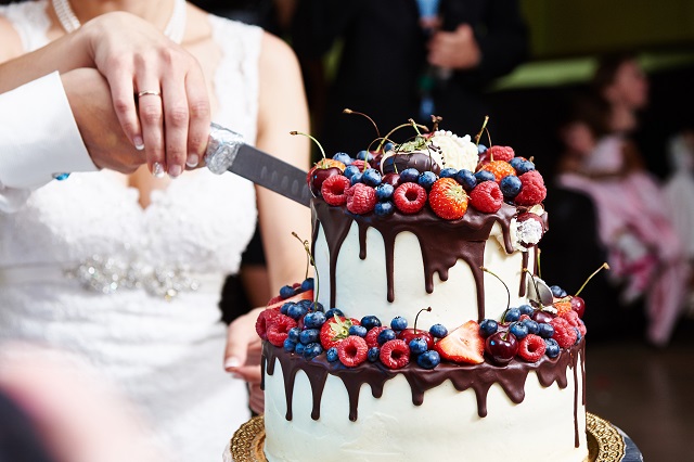 Cutting the wedding cake with berries on banquet