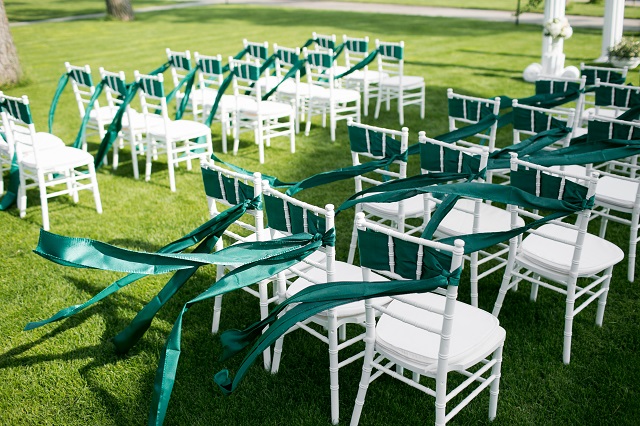 White wedding chairs with green ribbon outdoors
