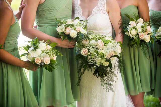 A candid photo of bride and her bridesmaids wearing light green bridesmaid dresses and holding a gorgeous bouquet. White and pink roses with baby's breath and green accents.